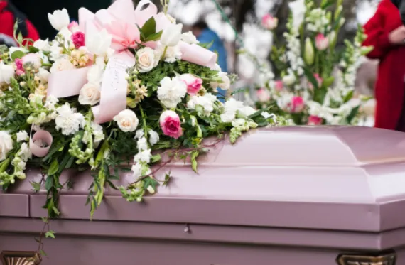 Cercueil en métal rose avec raquette de fleurs sur le dessus
