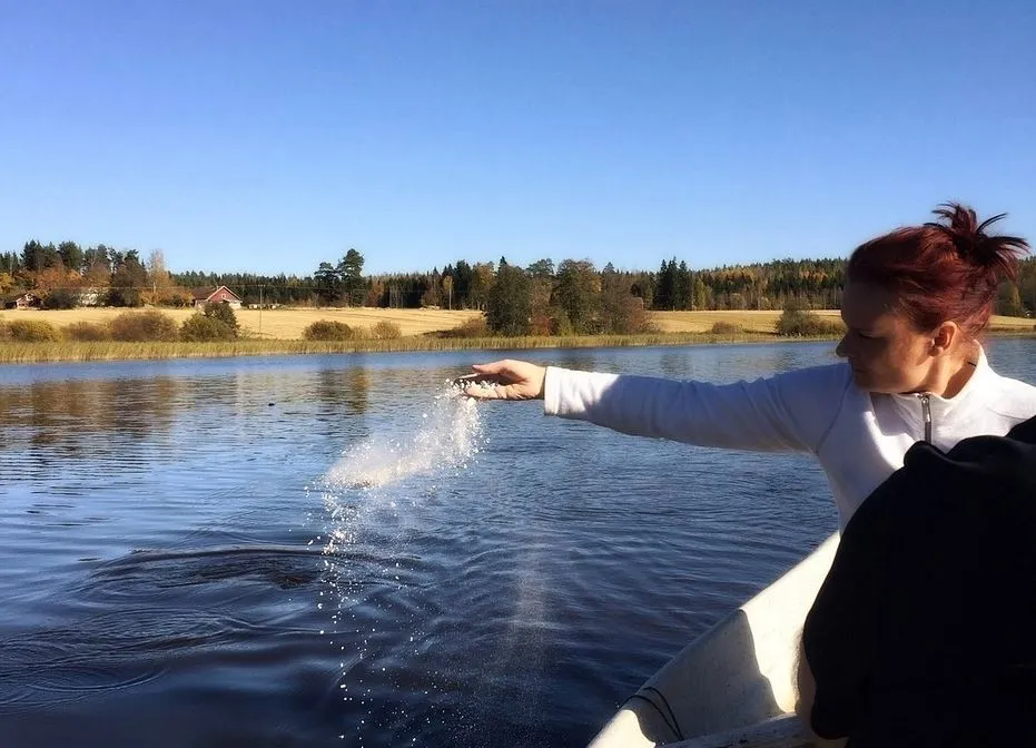 Femme sur une barque en tain de disperser des cendres dans un lac